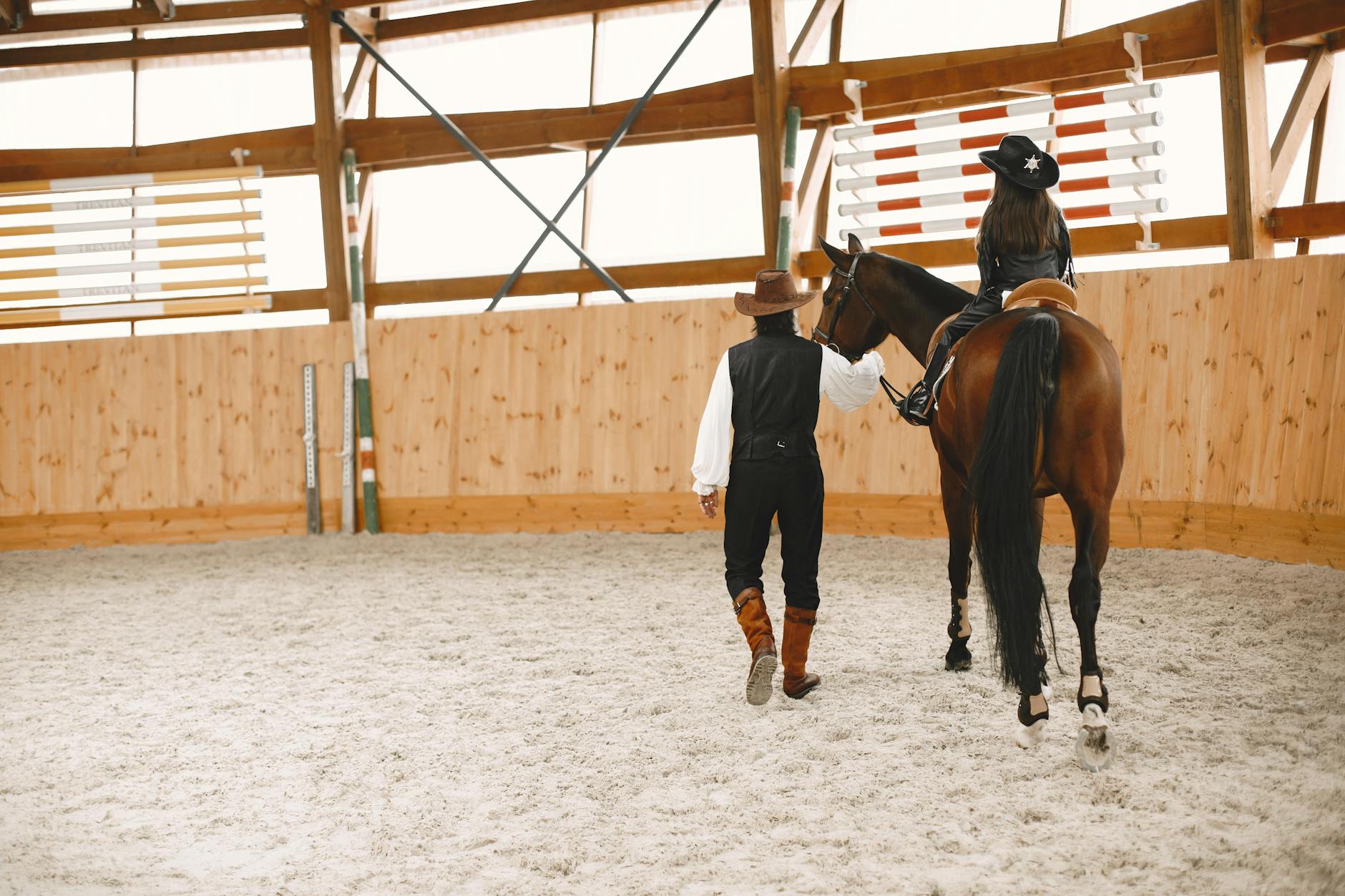 Instruktor w kowbojskim kapeluszu prowadzi dziewczynkę na koniu w hali