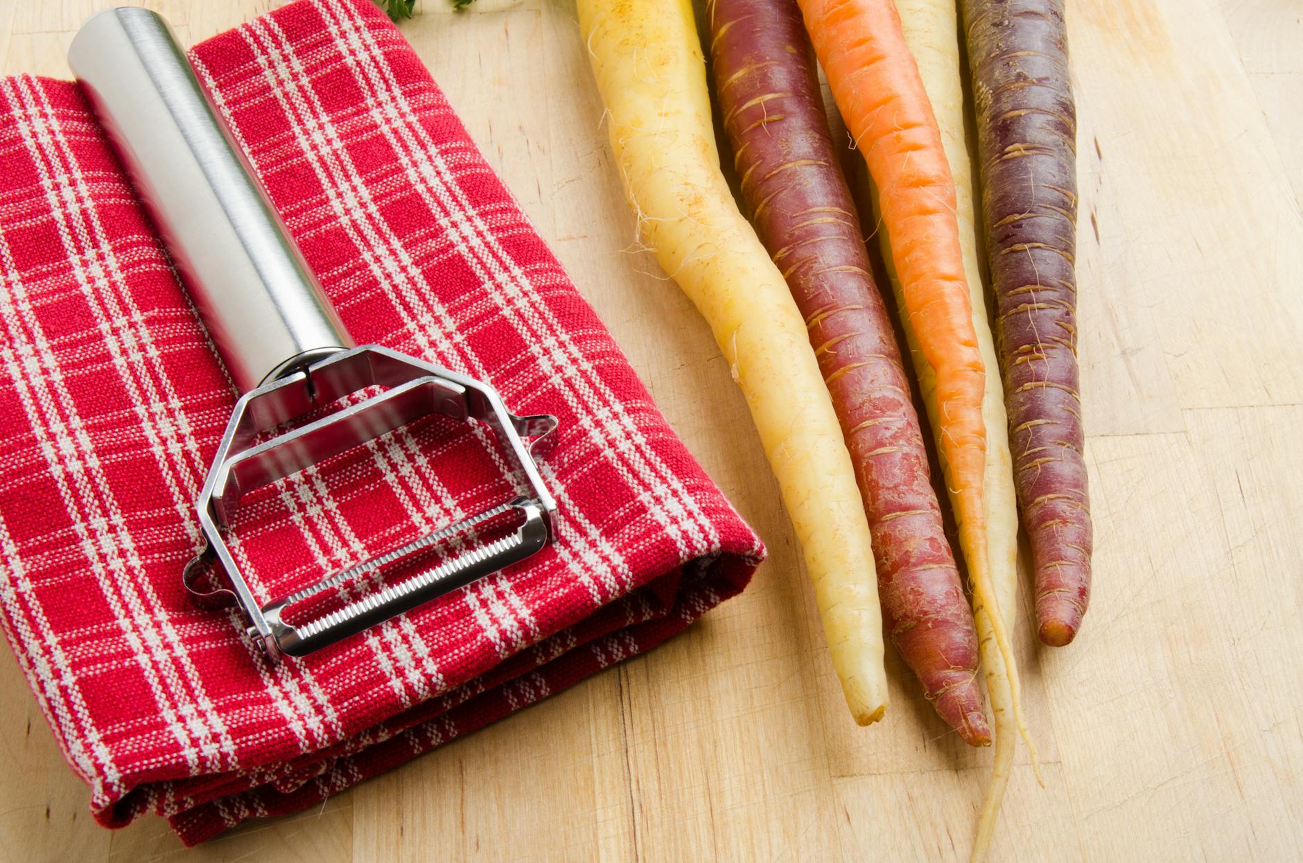Różnokolorowe marchewki i obieraczka na czerwonej kraciastej ściereczce