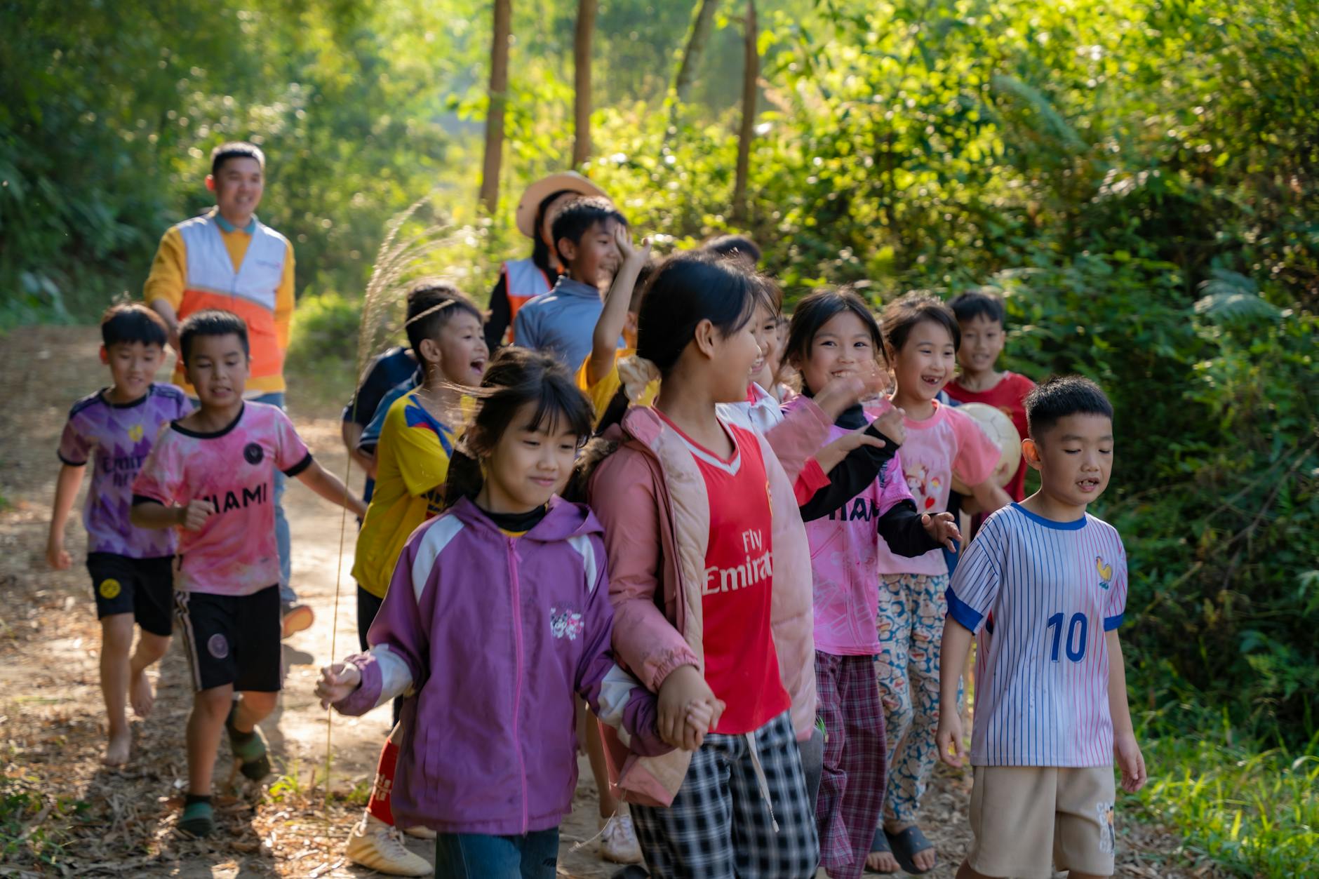 Grupa uśmiechniętych dzieci idzie leśną ścieżką w słoneczny dzień