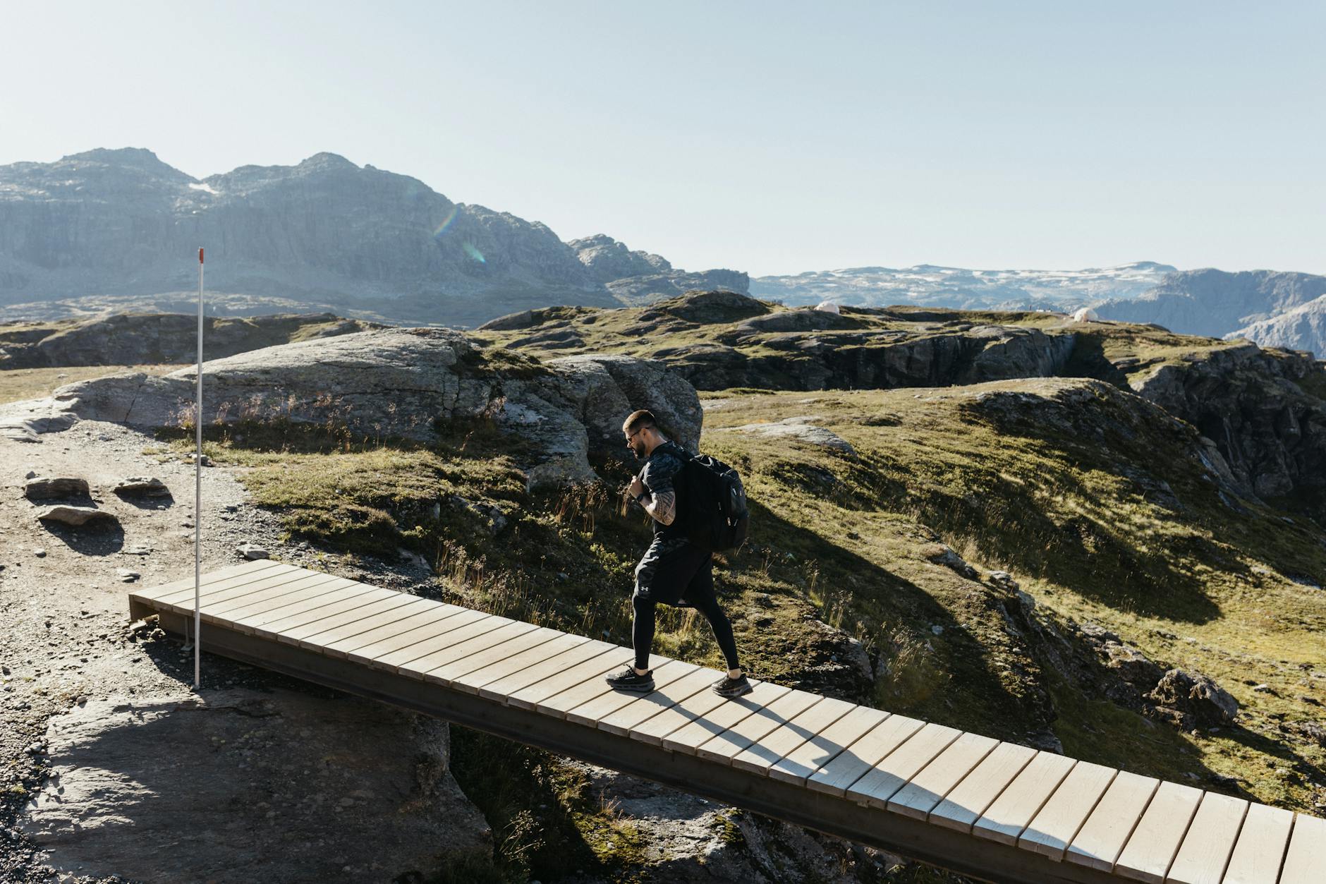 Turysta z plecakiem idzie po górskiej kładce w słoneczny dzień